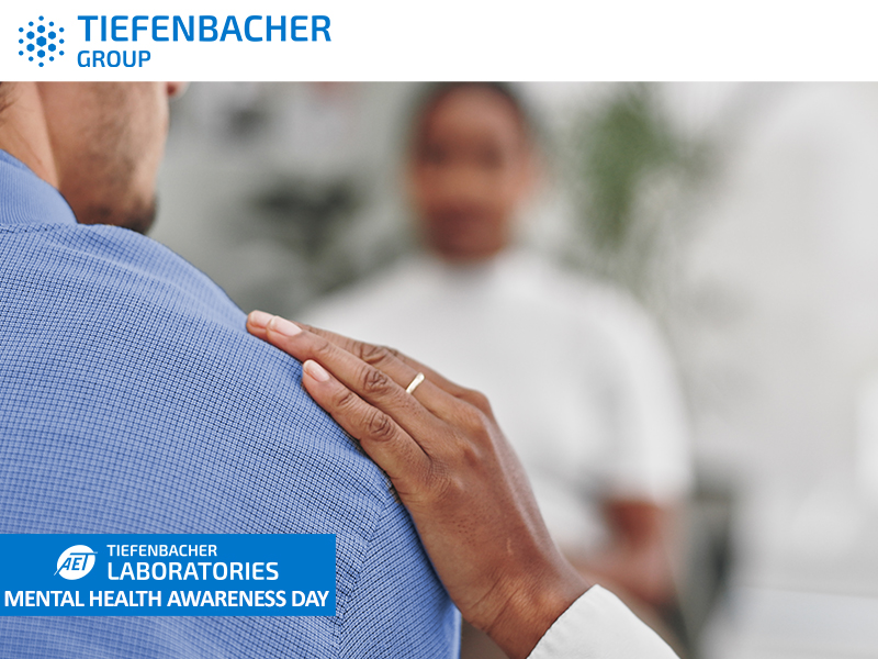 Tiefenbacher Group - A person gently places their hand on another's shoulder, offering support. The image promotes Mental Health Awareness Day and features the Tiefenbacher Group and Laboratories logos, reflecting their commitment to pharmaceutical healthcare solutions.