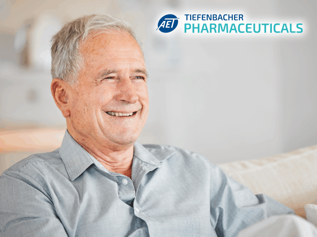 Tiefenbacher Group - An older man with gray hair smiles while sitting on a couch, wearing a light gray shirt. The logo and name "AET Tiefenbacher Pharmaceuticals," a family-owned pharmaceutical company, is visible in the upper right corner.