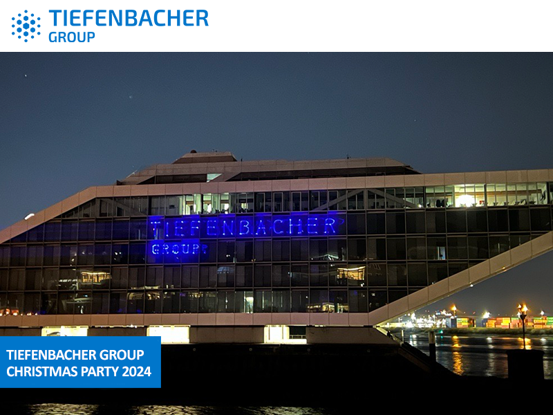 Tiefenbacher Group - Modern glass office building with blue neon "Tiefenbacher Group" sign illuminated at night by the water, city lights in the background. A family-owned pharmaceutical company specializing in finished dosage forms. Text overlay: "TIEFENBACHER GROUP CHRISTMAS PARTY 2024.
