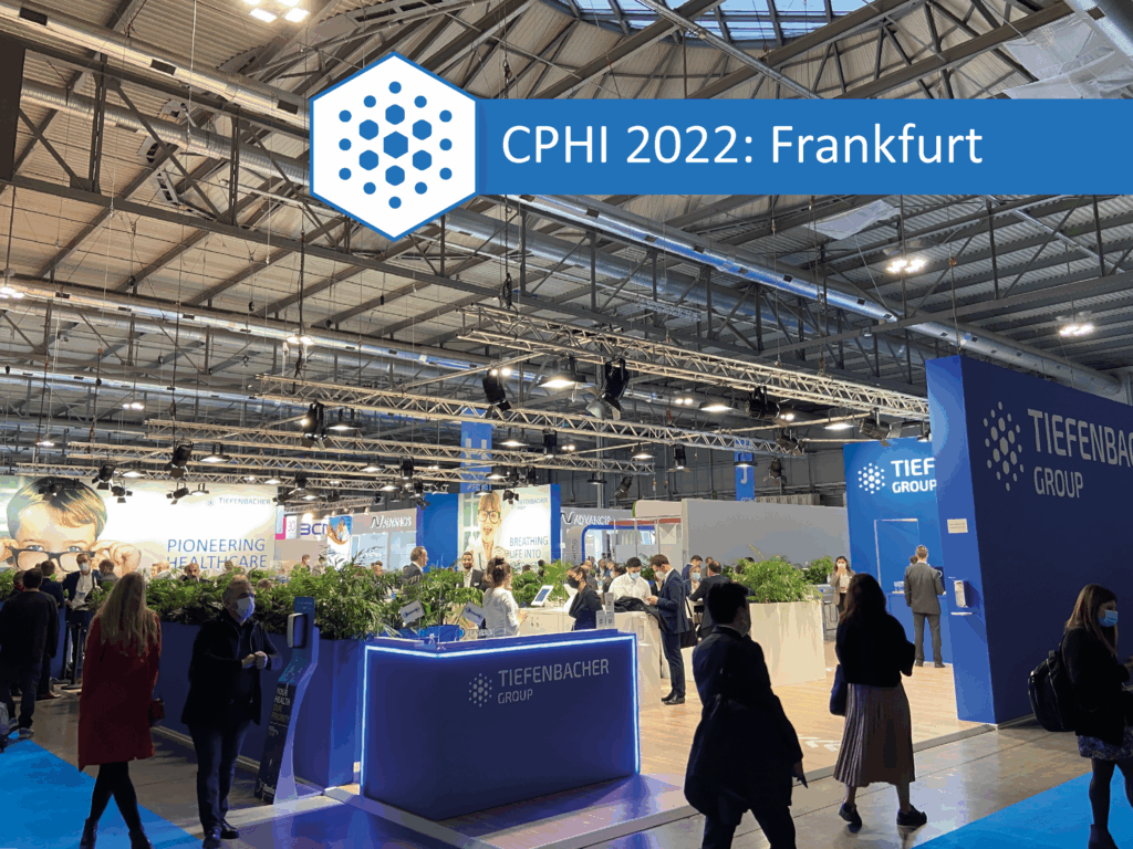 Tiefenbacher Group - Exhibition hall at CPHI 2022 in Frankfurt, featuring the Tiefenbacher Group booth—a family-owned pharmaceutical company specializing in finished dosage forms and API distribution. Bright lighting and displays create a lively atmosphere.
